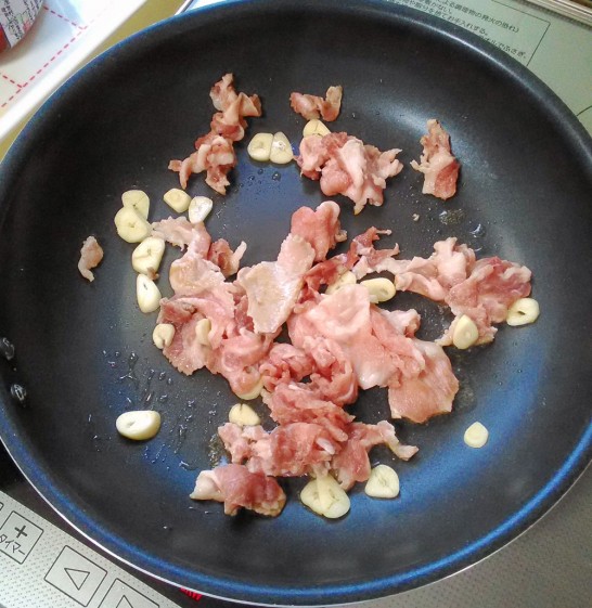 熱く熱したフライパンでニンニクと豚肉を炒める